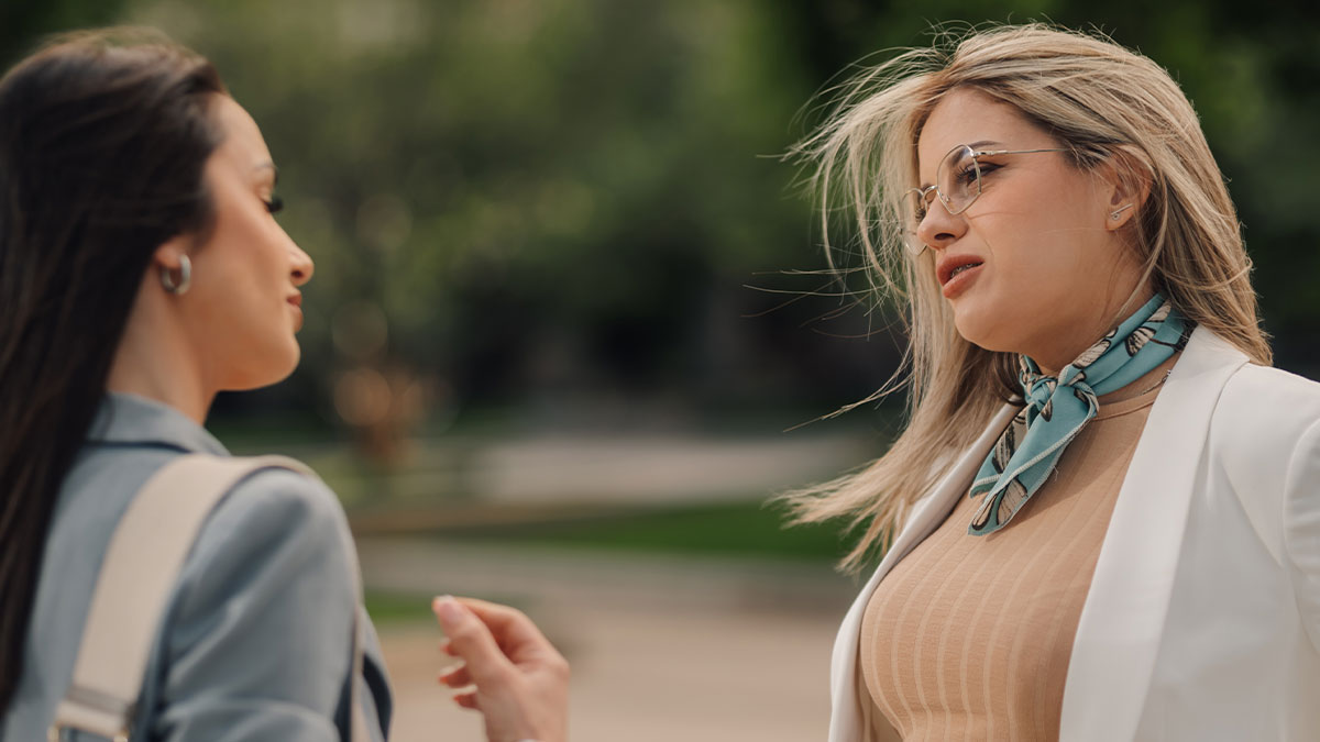 Two women engaged in a tense conversation outdoors, illustrating a woman stunned after ex-husbandu2019s girlfriend demands name change.
