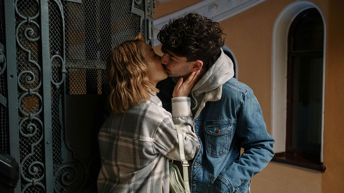 Young couple kissing outside near vintage iron gate, illustrating affair pregnancy and boyfriend conflict story.