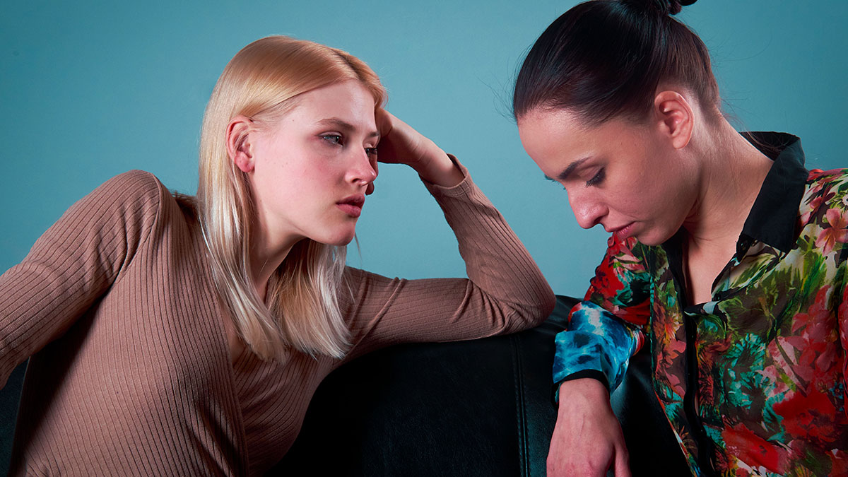 Two women having a serious conversation on a couch, illustrating tension around body count discussion.