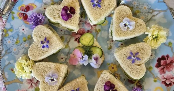 Heart-shaped tea sandwiches decorated with edible flowers on a floral plate for a jam and scones tea party challenge.