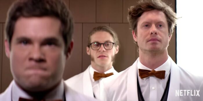 Three men in white tuxedos with brown bow ties, appearing serious in a scene from Netflix movies that were letdowns.