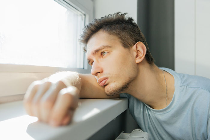 Young man looking out the window with a sad expression, reflecting on a destitute fiance relationship. Young man looking out the window with a sad expression, reflecting on a destitute fiance relationship.