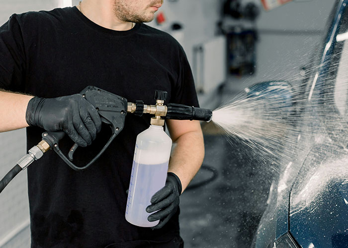 Man in black shirt using spray tool to clean car surface, illustrating boss impact on flexible hours at work. Man in black shirt using spray tool to clean car surface, illustrating boss impact on flexible hours at work.