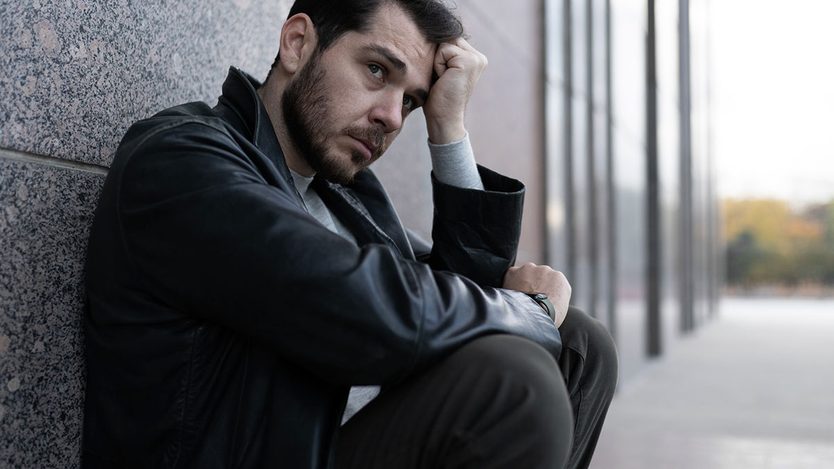 Man in a black jacket sitting against a wall looking contemplative, reflecting on life in prison challenges.