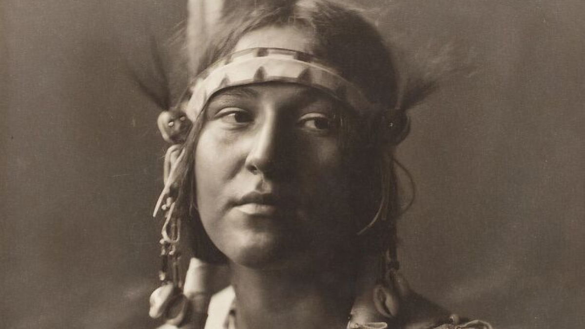Portrait of a Native tribeswoman from the 1900s wearing traditional headgear, capturing the strength of Native tribes.