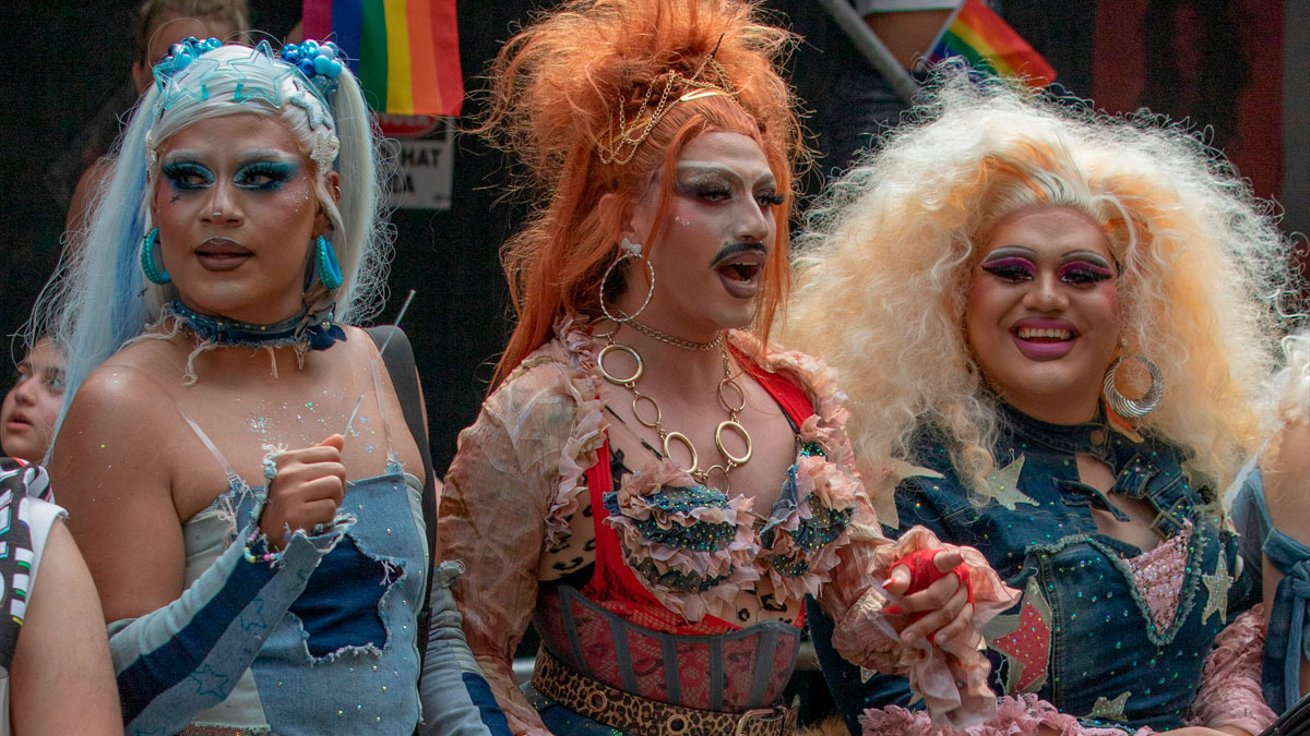 Two amazing drag queens in colorful makeup and outfits confidently posing during a lively outdoor event.