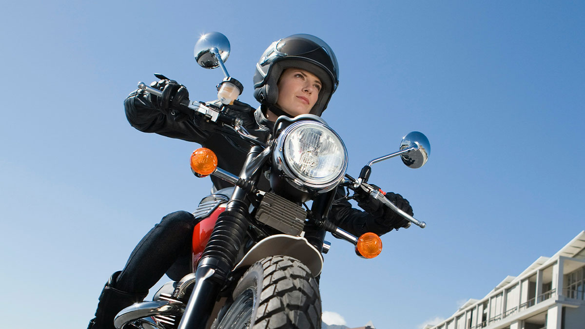 Teen confident on motorcycle wearing helmet and leather jacket under clear blue sky, ready for a ride.