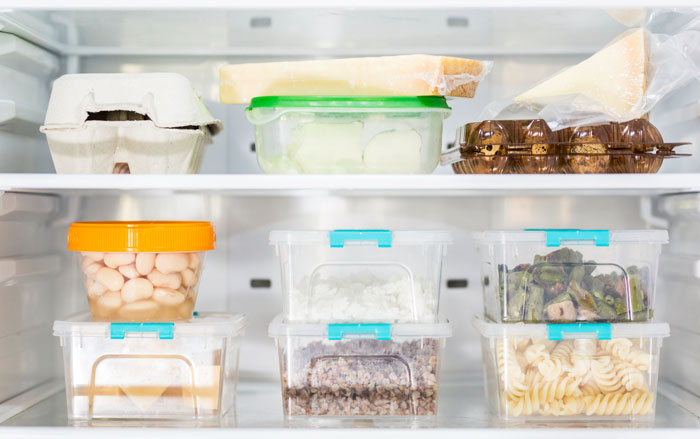 Organized fridge shelves with plastic containers holding various leftovers, highlighting leftover pasta and food theft concern.
