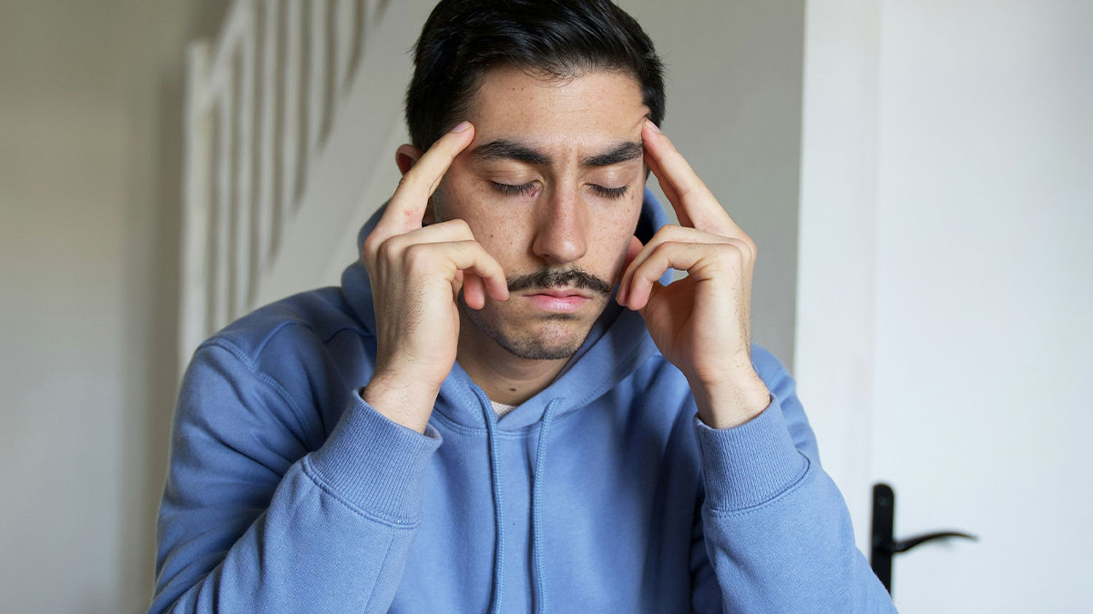 Man in a blue hoodie looking worried and stressed, holding his temples, reacting to a shady loan request from a friend.