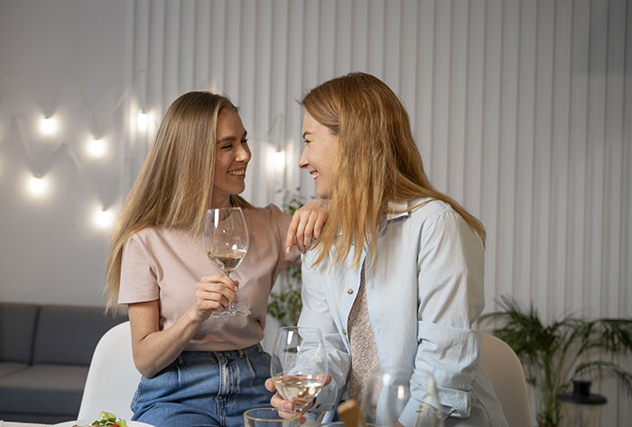 Two women smiling and socializing over wine, depicting confusion and tension after a test involving boyfriend’s sister. Two women smiling and socializing over wine, depicting confusion and tension after a test involving boyfriend’s sister.