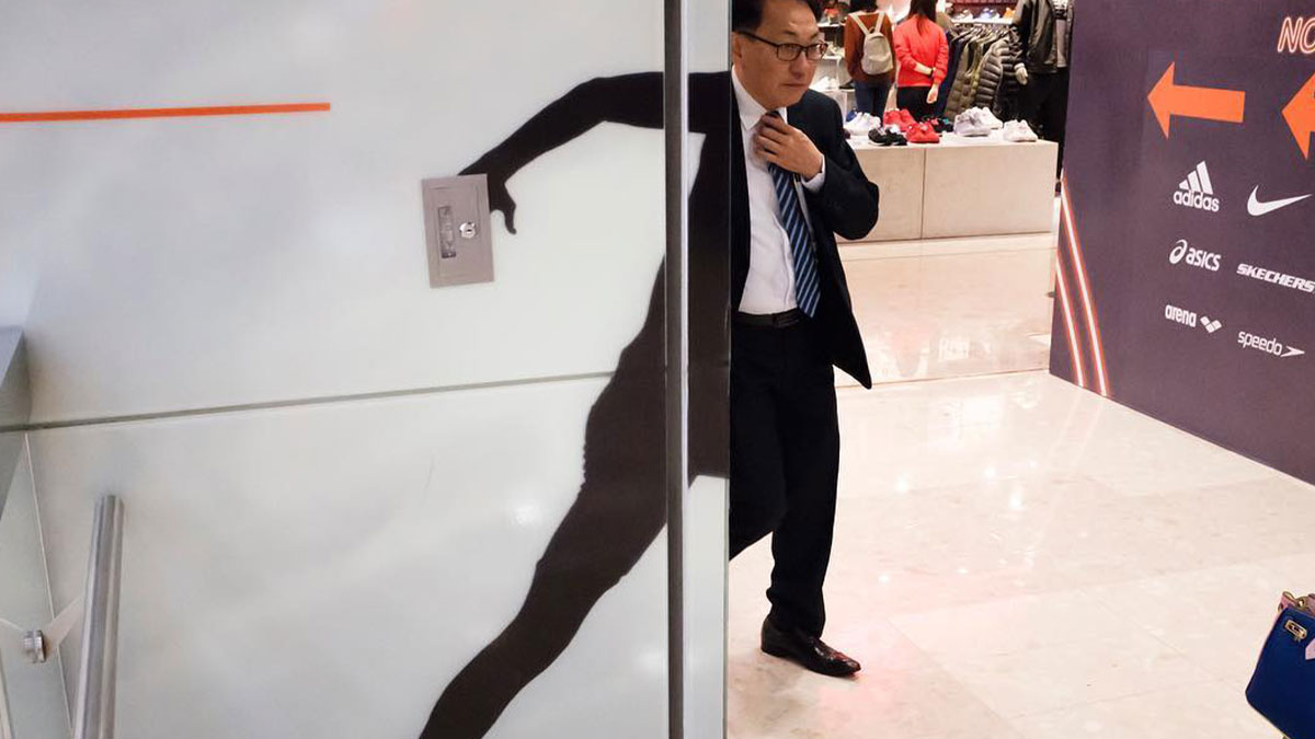 Man adjusting his tie standing beside a wall shadow creating an unbelievable street coincidence in a public shopping area.