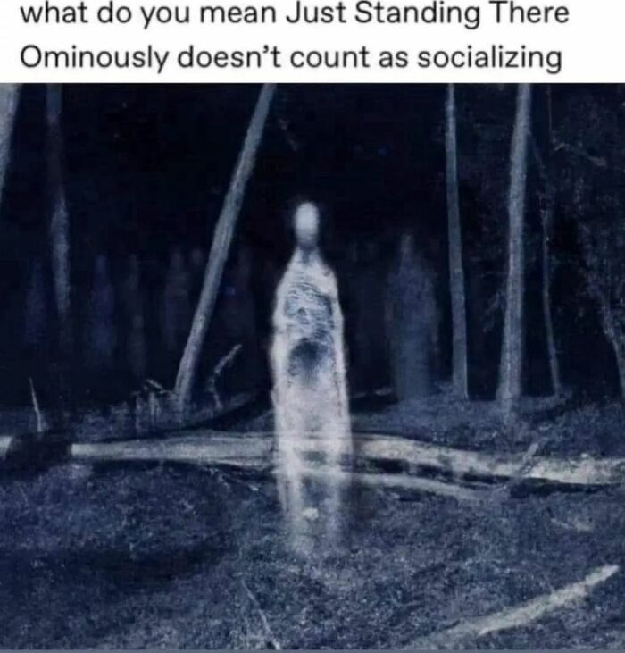Ghostly figure standing in dark forest with text about standing ominously not counting as socializing, creepy funny meme.