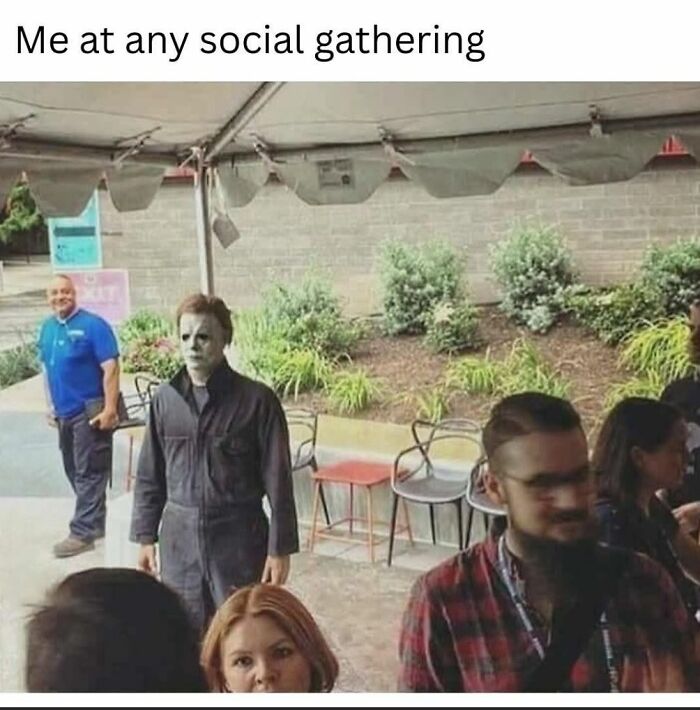 Person wearing a creepy Halloween mask standing awkwardly at a social gathering, capturing a creepy but funny meme moment.
