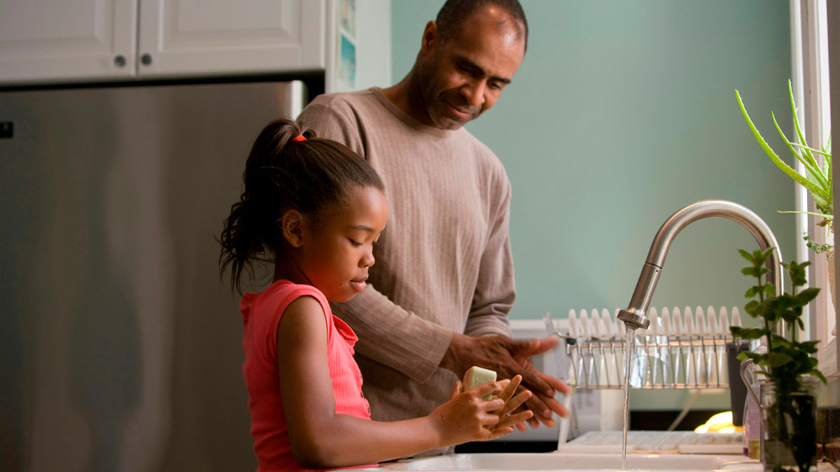 Father and daughter washing their hands together in the kitchen, showcasing parenting moments amid everyday chaos.