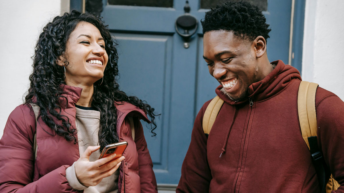 Two friends smiling and laughing together outside, enjoying a moment that could break your doomscrolling cycle.