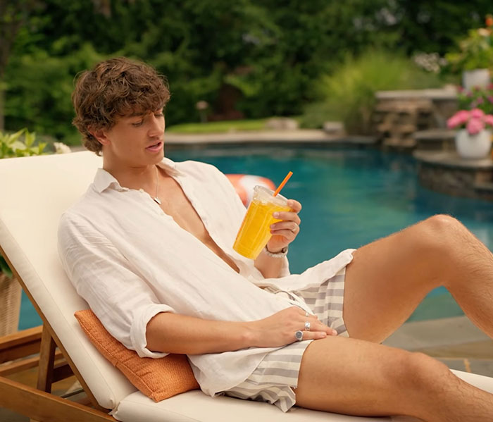 Young man relaxing by the pool with a drink, illustrating a scene related to genetics and woke outrage in an ad campaign. Young man relaxing by the pool with a drink, illustrating a scene related to genetics and woke outrage in an ad campaign.