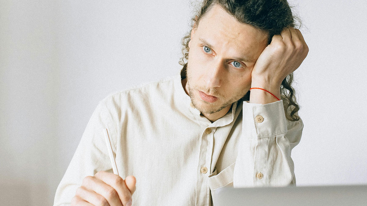Young intern looking stressed and exhausted while working on a laptop after coworker brings cupcakes at office.