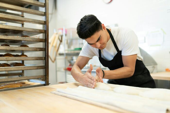 Young male baker shaping dough in a bakery, illustrating gender-based double standards in professional roles.