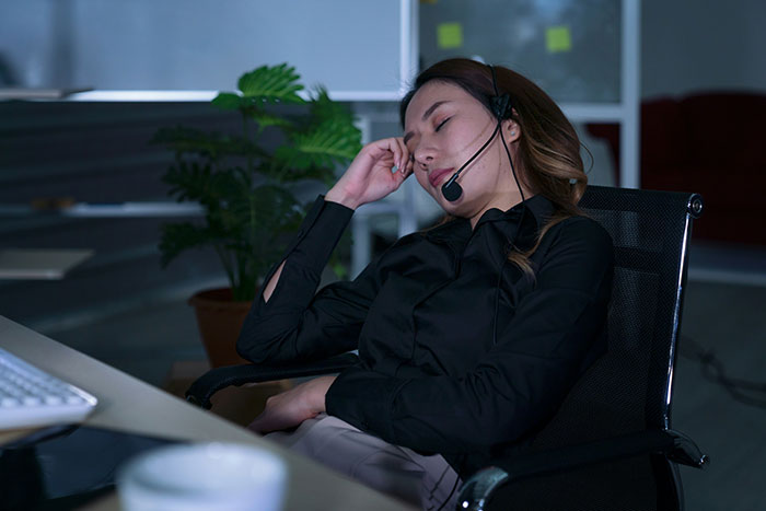 Tired woman wearing headset sitting at desk in dark office, reflecting quiet life with two kids and bonus stepdaughter conflict. Tired woman wearing headset sitting at desk in dark office, reflecting quiet life with two kids and bonus stepdaughter conflict.