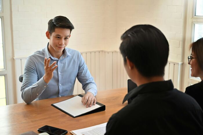 Man using unhinged hacks during a job interview, confidently explaining points to two interviewers at a wooden table.