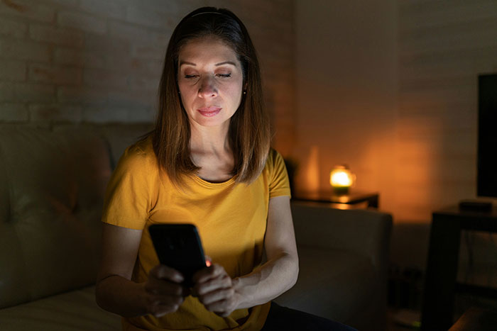 Mom-to-be reading strange text about fiancé on phone, sitting in dimly lit room, looking concerned and thoughtful. Mom-to-be reading strange text about fiancé on phone, sitting in dimly lit room, looking concerned and thoughtful.