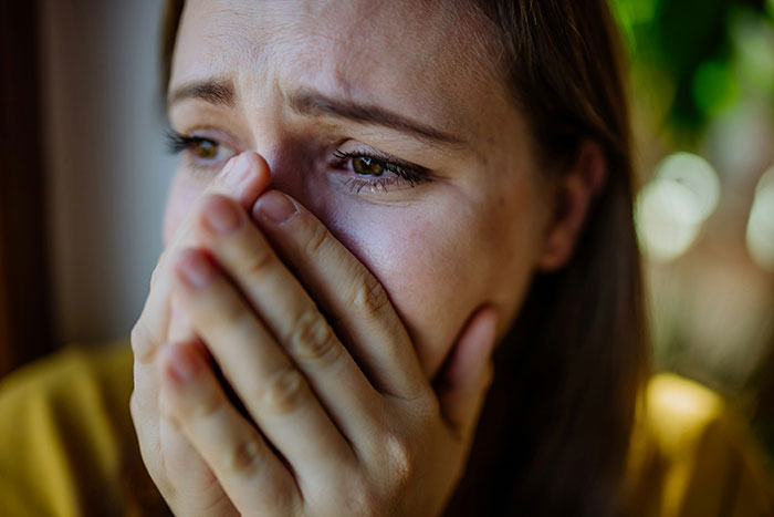 Close-up of a distressed woman covering her mouth, reflecting frustration over cat duties and roommate conflict.