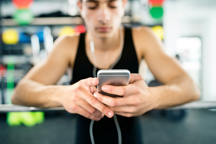 Teen focused on phone with earbuds at gym, representing incident of lady grabbing teen's phone during photo. Teen focused on phone with earbuds at gym, representing incident of lady grabbing teen's phone during photo.