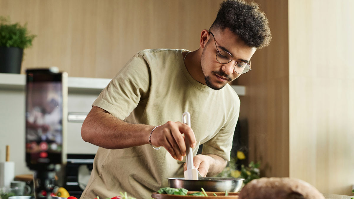 Young man cooking dinner in kitchen, focused on preparing food with spatula, demonstrating dinner he made for girlfriend