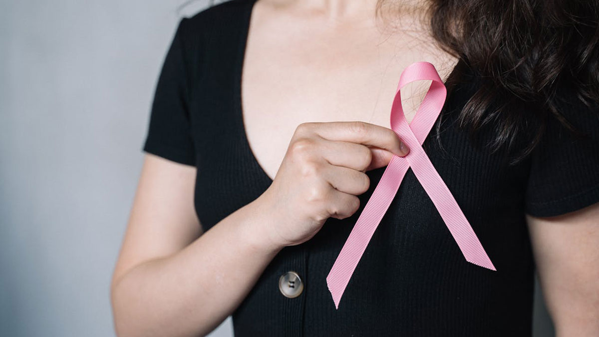 Woman in a black shirt holding a pink ribbon symbolizing good news and hope in health awareness campaigns.