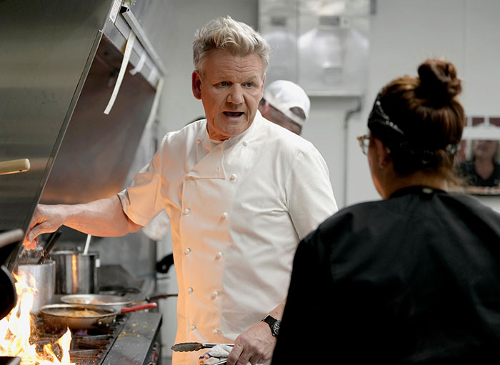 Celebrity chef in a kitchen with flames, reflecting intensity unrelated to Ellen DeGeneres bullying controversy reignited claims.