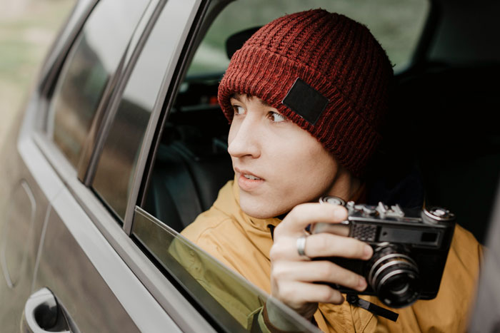 Teen holding vintage camera inside car, exploring portable darkroom concept during surplus auction adventure.