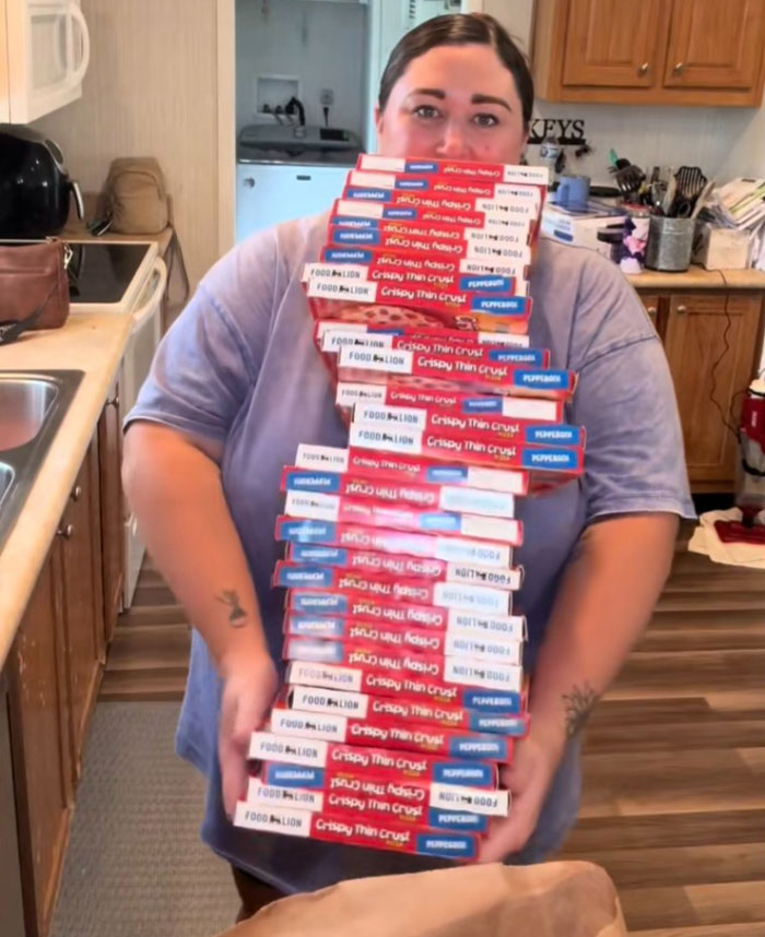 Woman in kitchen holding a large stack of frozen pizzas as part of an American family grocery haul Woman in kitchen holding a large stack of frozen pizzas as part of an American family grocery haul