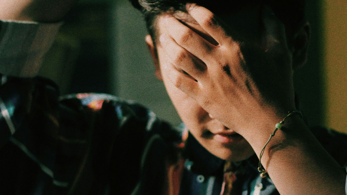 Young man covering his face, showing frustration and refusal related to babysitting siblings after feeling like a stranger.