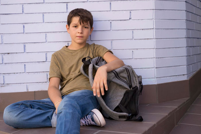 Young boy sitting on steps with backpack, looking thoughtful and upset, reflecting feelings of neglect in family conflict. Young boy sitting on steps with backpack, looking thoughtful and upset, reflecting feelings of neglect in family conflict.