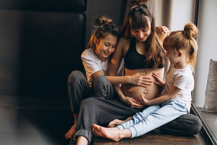 Pregnant lady sitting with her children, smiling and touching her baby bump in a warm family moment at home. Pregnant lady sitting with her children, smiling and touching her baby bump in a warm family moment at home.