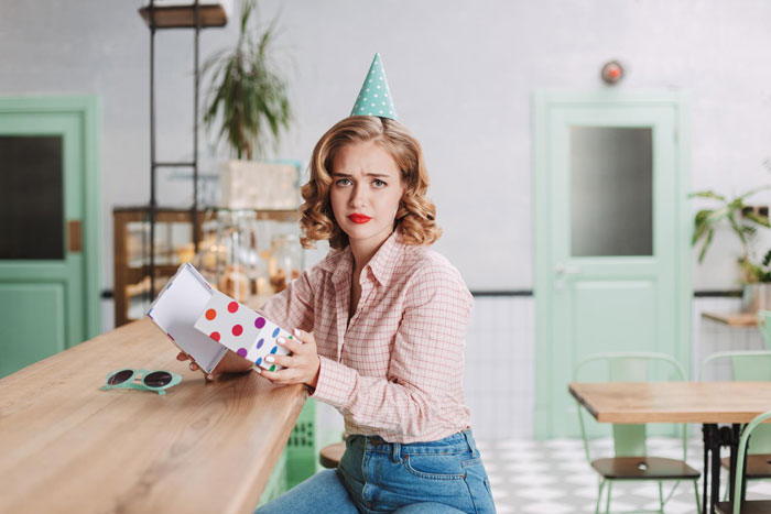 Young woman wearing a party hat at a birthday dinner, upset while holding a gift box, influencer filming conflict scene. Young woman wearing a party hat at a birthday dinner, upset while holding a gift box, influencer filming conflict scene.