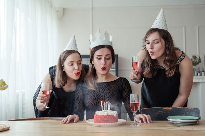Three women at a birthday dinner, one wearing a paper crown, with party hats and glasses of pink drink celebrating. Three women at a birthday dinner, one wearing a paper crown, with party hats and glasses of pink drink celebrating.