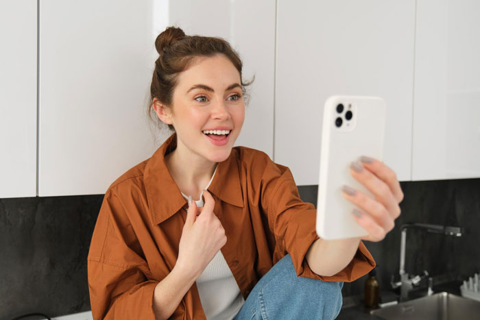 Young woman acting as self-proclaimed influencer filming herself with smartphone, looking excited in casual indoor setting. Young woman acting as self-proclaimed influencer filming herself with smartphone, looking excited in casual indoor setting.