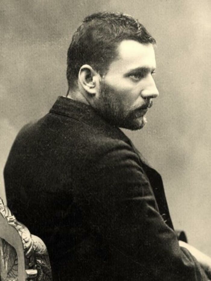 Victorian man with beard and short hair in a dark coat sitting on an ornate chair, classic handsome Victorian men portrait.