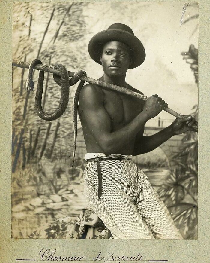 Victorian man with a hat, holding a snake on a stick, showcasing strength and charm in a vintage black and white photo.