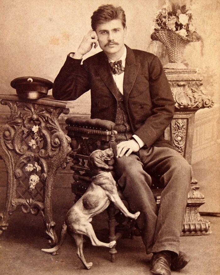 Vintage portrait of a handsome Victorian man with mustache sitting, accompanied by a small dog in a classic setting.