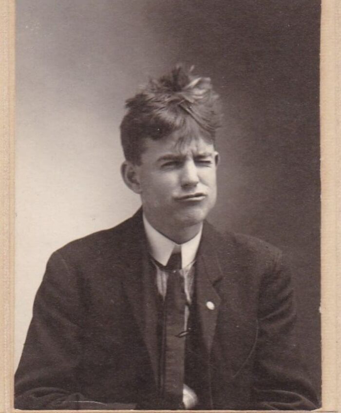 Young Victorian man with tousled hair wearing a suit making a playful facial expression in a vintage portrait.