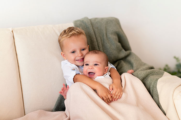 Two young siblings sitting on a couch wrapped in blankets, showing a caring babysitting moment. Two young siblings sitting on a couch wrapped in blankets, showing a caring babysitting moment.