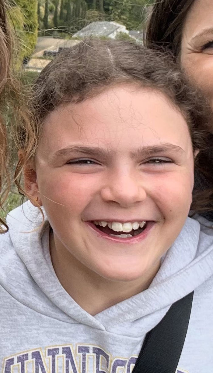 Smiling young girl wearing a gray hoodie outdoors, related to Minneapolis school attacker mother not cooperating with cops debate. Smiling young girl wearing a gray hoodie outdoors, related to Minneapolis school attacker mother not cooperating with cops debate.