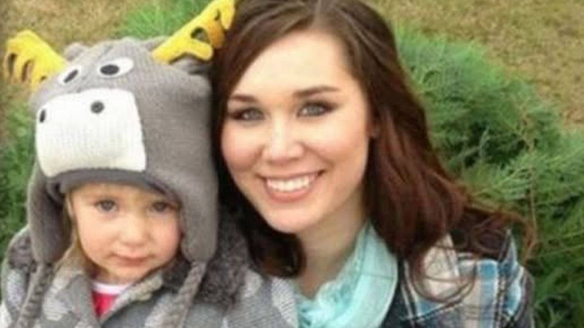 Young woman smiling with a child wearing a playful animal hat in an outdoor setting, unsettling images theme.