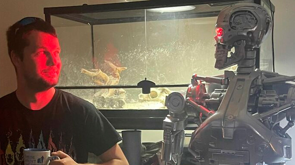 Man holding a cup smiling at a robot with red glowing eye, a scene that any man would be excited to see.