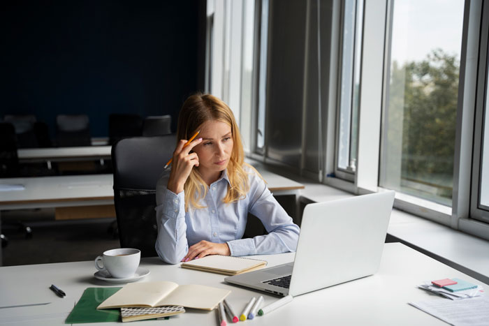 Young professional woman at office desk, looking concerned while working on laptop, illustrating toxic newbie conflict at work. Young professional woman at office desk, looking concerned while working on laptop, illustrating toxic newbie conflict at work.
