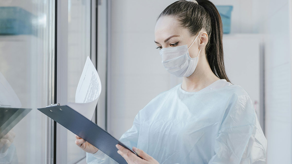 Woman in medical gown and mask reading documents on a clipboard showing person tired of fun facts requesting horrifying ones