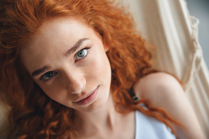 Close-up of a young woman with red curly hair and blue eyes, highlighting surprising body quirks that make you see yourself differently.
