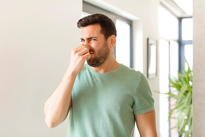 Man in green shirt holding nose indoors, illustrating surprising body quirks that may change how you see yourself.